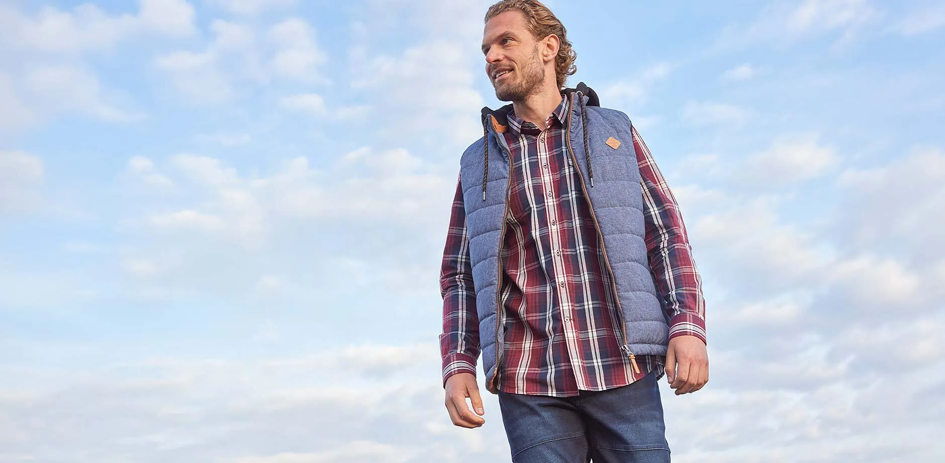 Chemise à carreaux, jean bleu et veste sans manches grise.