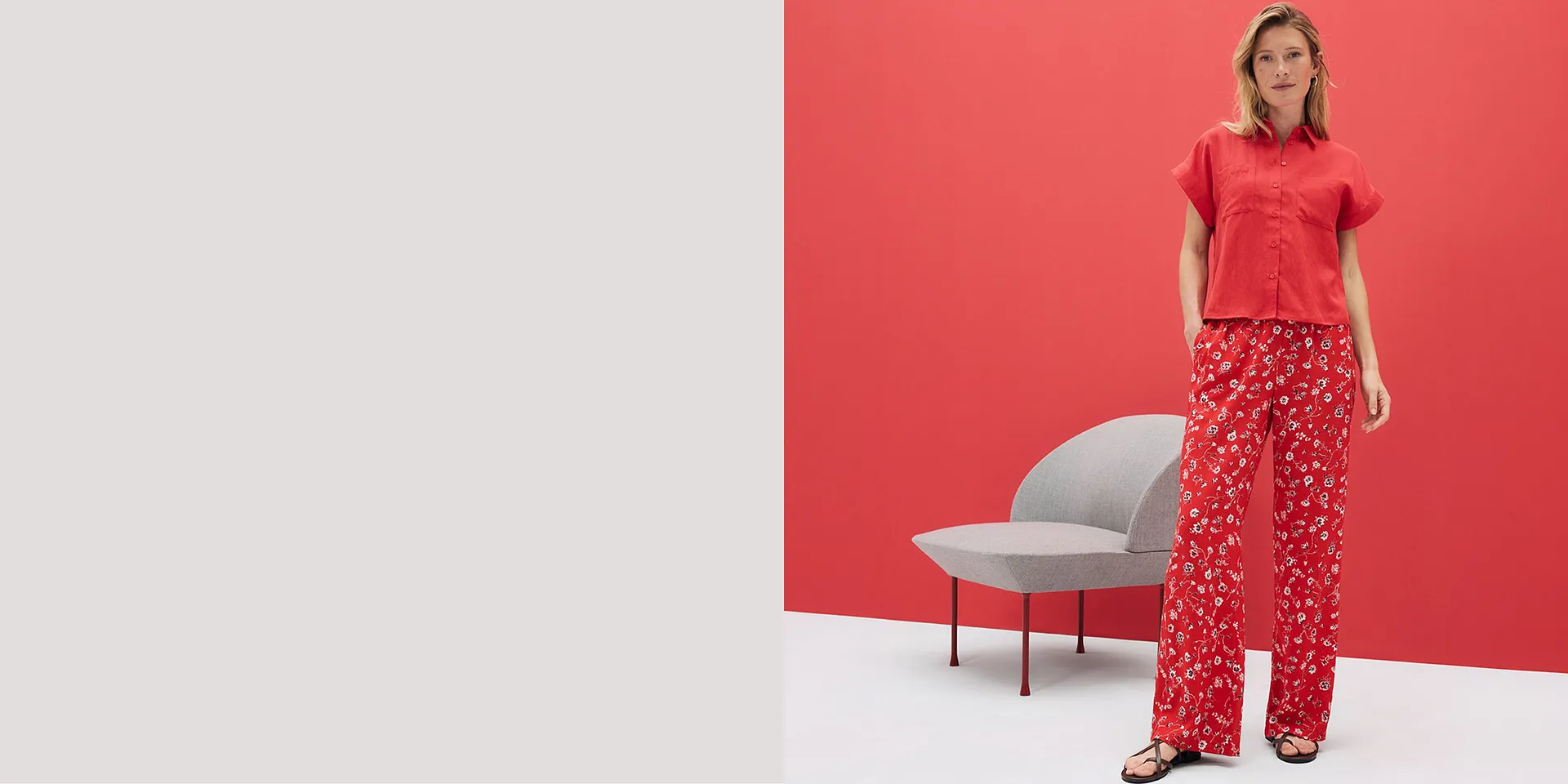 Chemisier rouge à manches courtes et pantalon fluide à motif floral. Une tenue estivale sur un fond rouge lumineux.