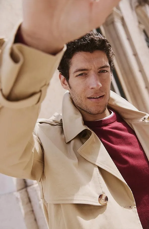 Trench-coat beige élégant par dessus un pull rouge bourgogne.