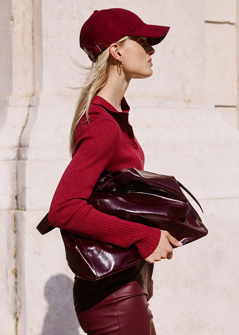 Look chic en rouge bourgogne : pull en maille, pantalon enduit, casquette de baseball et sac à main verni.