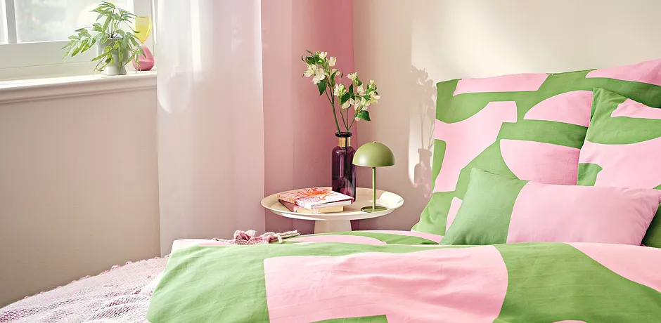 La parure de lit en rose et vert apporte une fraîcheur estivale dans la chambre à coucher éclairée par un rayon de soleil.