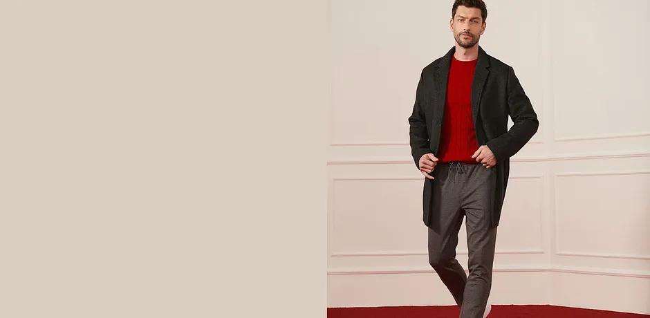 Manteau en laine fonc&eacute;, pull rouge et pantalon gris pour un look &eacute;l&eacute;gant.