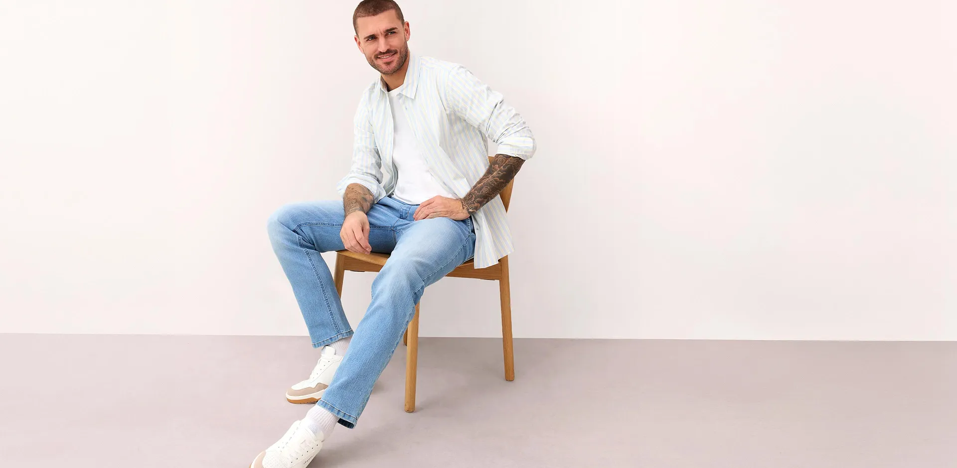 Chemise blanche ray&eacute;e, jean bleu clair et sneakers blanches.