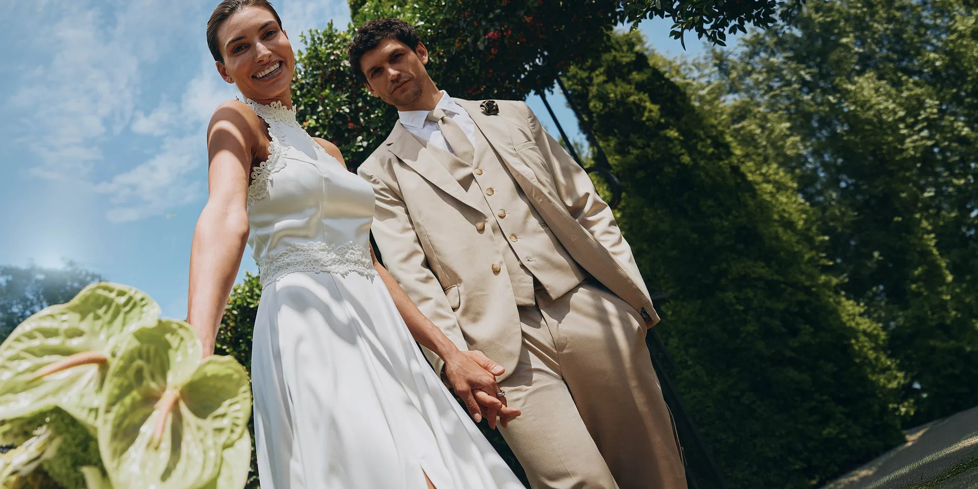Jeunes mari&eacute;s par une belle journ&eacute;e ensoleill&eacute;e : la mari&eacute;e porte une robe blanche, le mari&eacute; un costume de couleur beige.