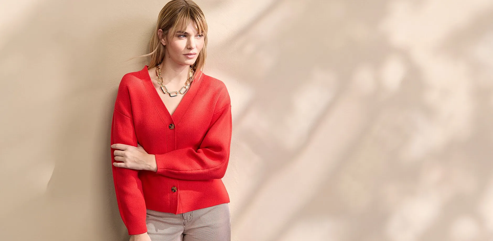 Un gilet en maille rouge &eacute;clatant avec d&eacute;collet&eacute; en V et boutons, rehauss&eacute; d'un gros collier de couleur dor&eacute;e.