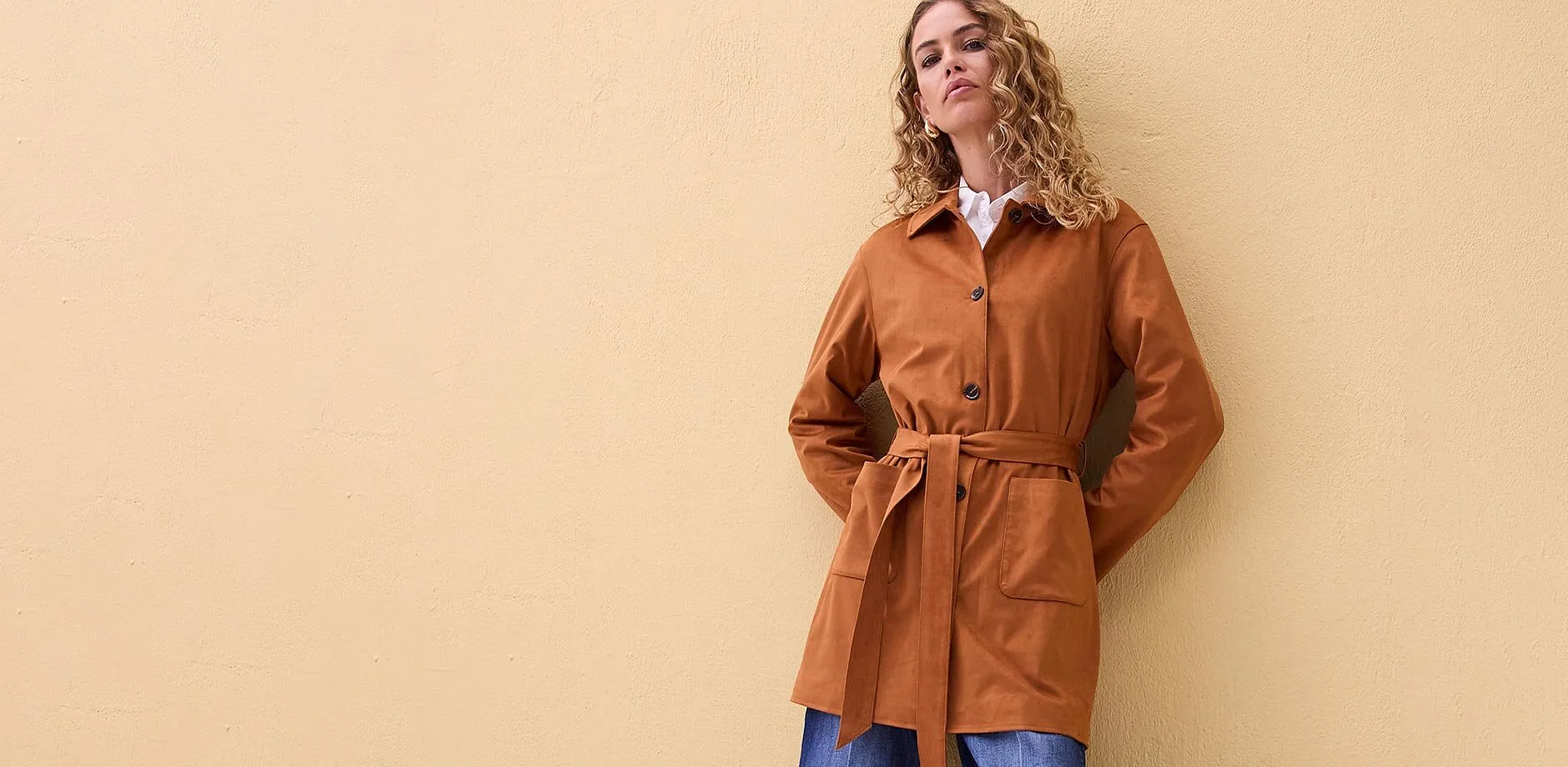 Manteau de couleur rouille avec ceinture, associ&eacute; &agrave; un chemisier blanc.