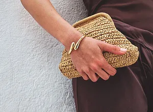 Robe marron élégante assortie d'un petit sac estival en paille. Un bracelet couleur dorée ajoute une touche de style.