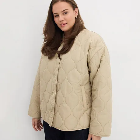 Veste matelassée beige avec boutons, associée à un pantalon foncé.