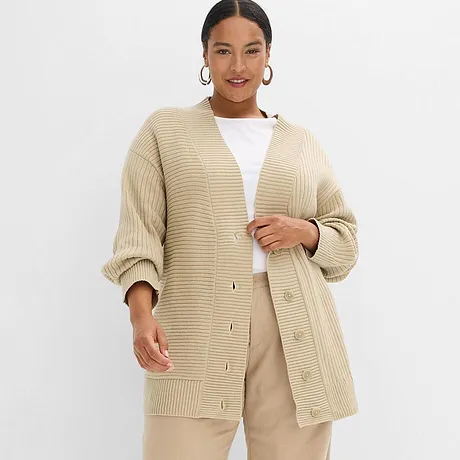 Cardigan oversize beige en grosse maille, associé à un top blanc et un pantalon beige clair.