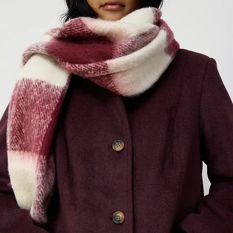 Manteau bordeaux élégant associé à une grosse écharpe douillette rouge et blanche.