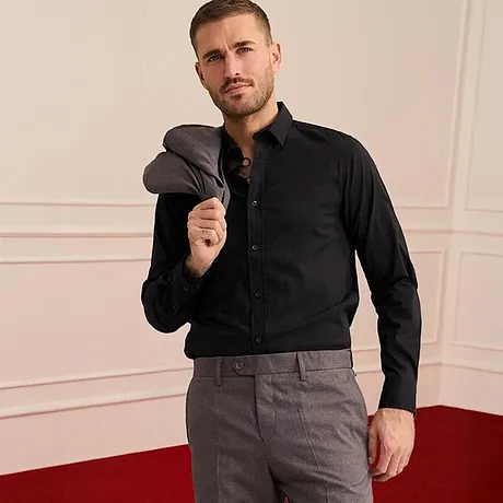 Chemise noire, pantalon gris et veste par dessus l'épaule.