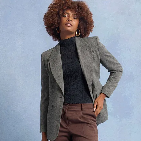 Blazer gris sur un pull à col roulé foncé, associé à un pantalon marron.