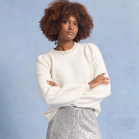 Pull blanc avec col décoré, associé à une jupe à paillettes de couleur argentée. 