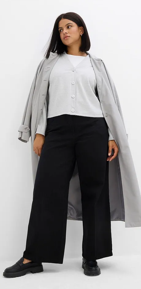 Manteau gris sur un chemisier blanc et un pantalon large noir.