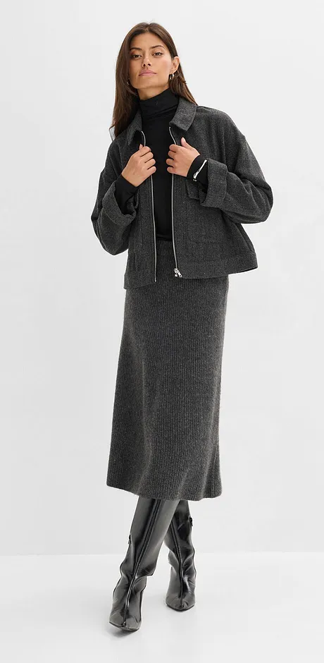 Jupe en maille grise, pull à col roulé noir, veste courte et bottes hautes.