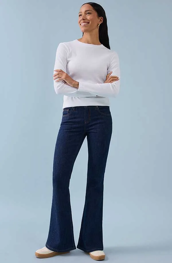 T-shirt blanc à manches longues associé à un pantalon bleu foncé à pattes d'eph pour un look chic et intemporel.