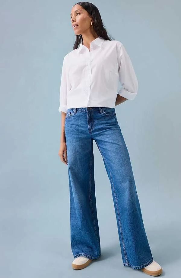 Chemisier blanc, jean bleu à jambes larges et chaussures blanches.