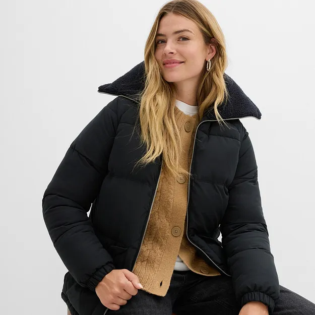 Veste noire d'hiver avec col montant par dessus un pull en maille jaune et un T-shirt blanc.