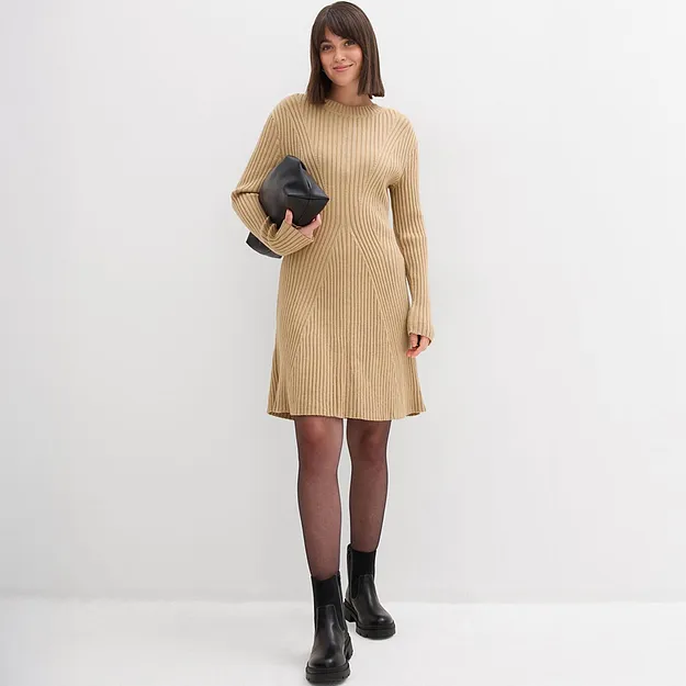 Robe en maille &eacute;l&eacute;gante de couleur beige avec encolure ronde et manches longues. Une pochette noire compl&egrave;te la tenue. 