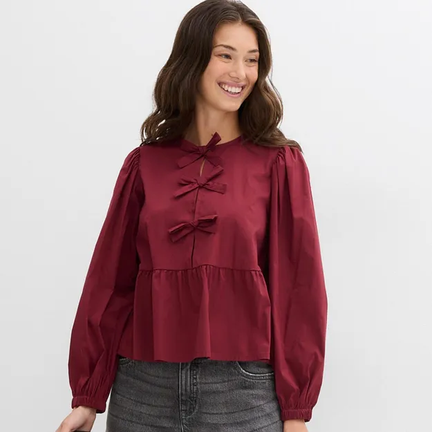 Blouse rouge bourgogne avec n&oelig;ud au col, manches bouffantes et ruch&eacute;s.