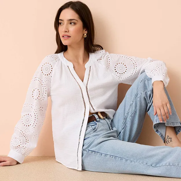 Blouse blanche &agrave; broderie anglaise avec manches longues, associ&eacute;e &agrave; un jean bleu clair et une ceinture.