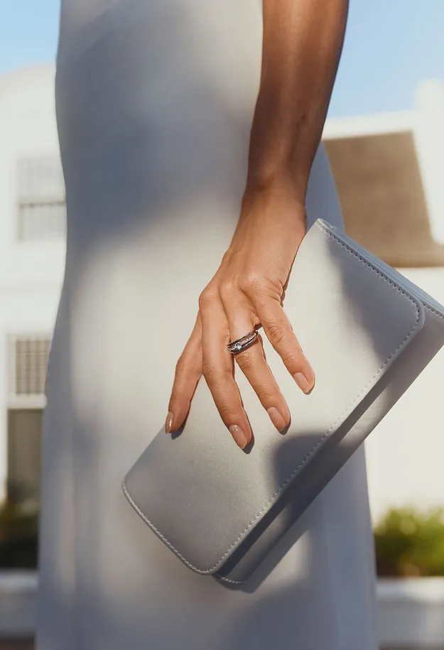 Robe blanche associ&eacute;e &agrave; une pochette claire et une bague raffin&eacute;e.