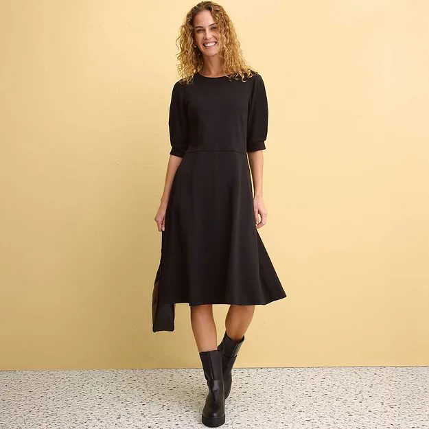 Robe midi noire &eacute;l&eacute;gante avec manches bouffantes, port&eacute;e avec des bottes noires.