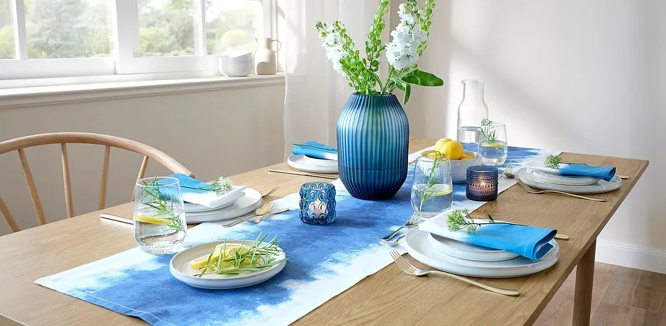 Un chemin de table bleu décore la table de la salle à manger, en contraste avec des assiettes blanches et des accessoires colorés.