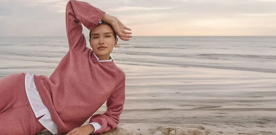 Femme en pull rose en maille à capuche au bord de l'eau, un look détente et douillet.