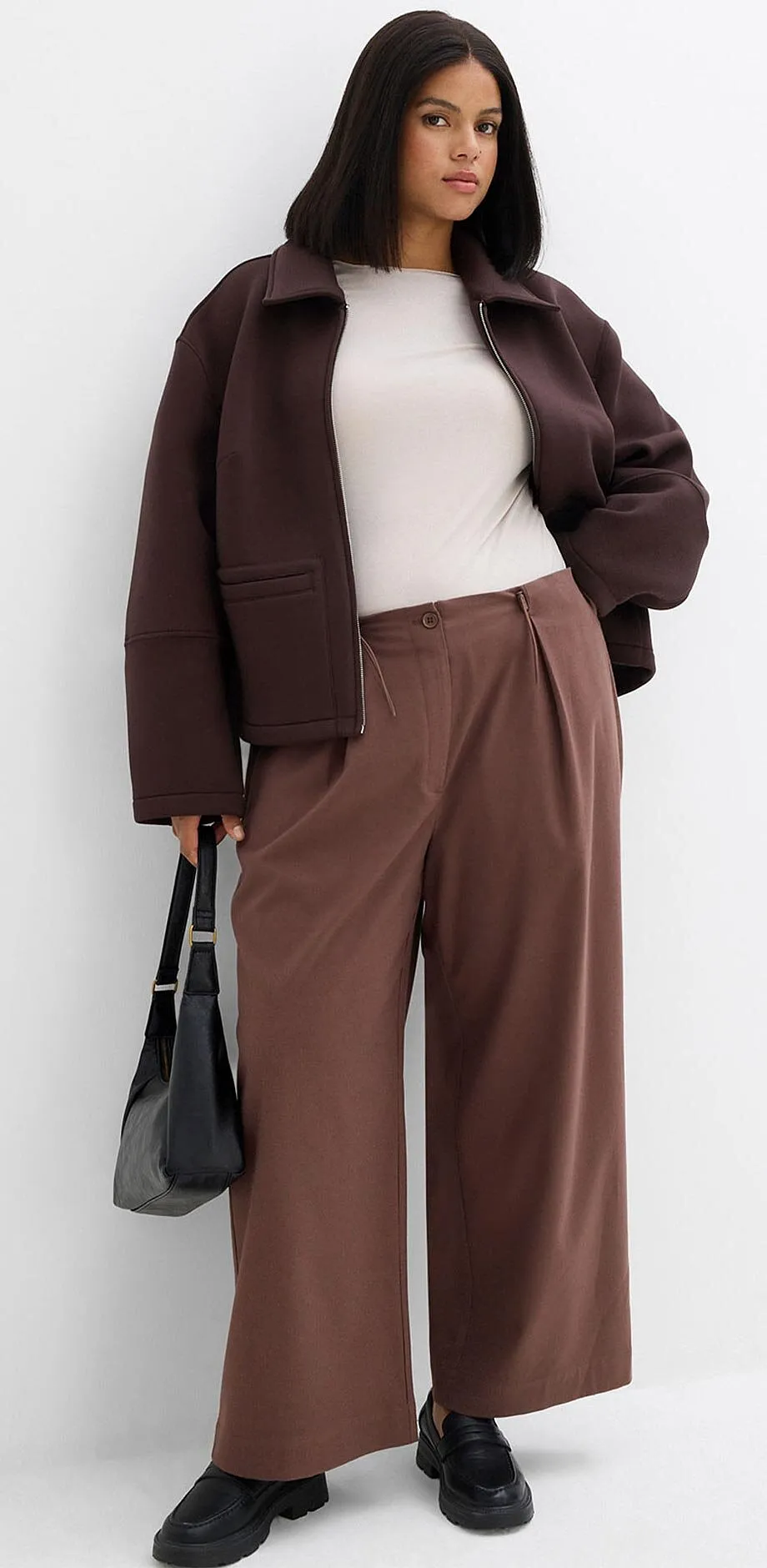 Veste marron, top blanc et pantalon large dans des tons terreux.