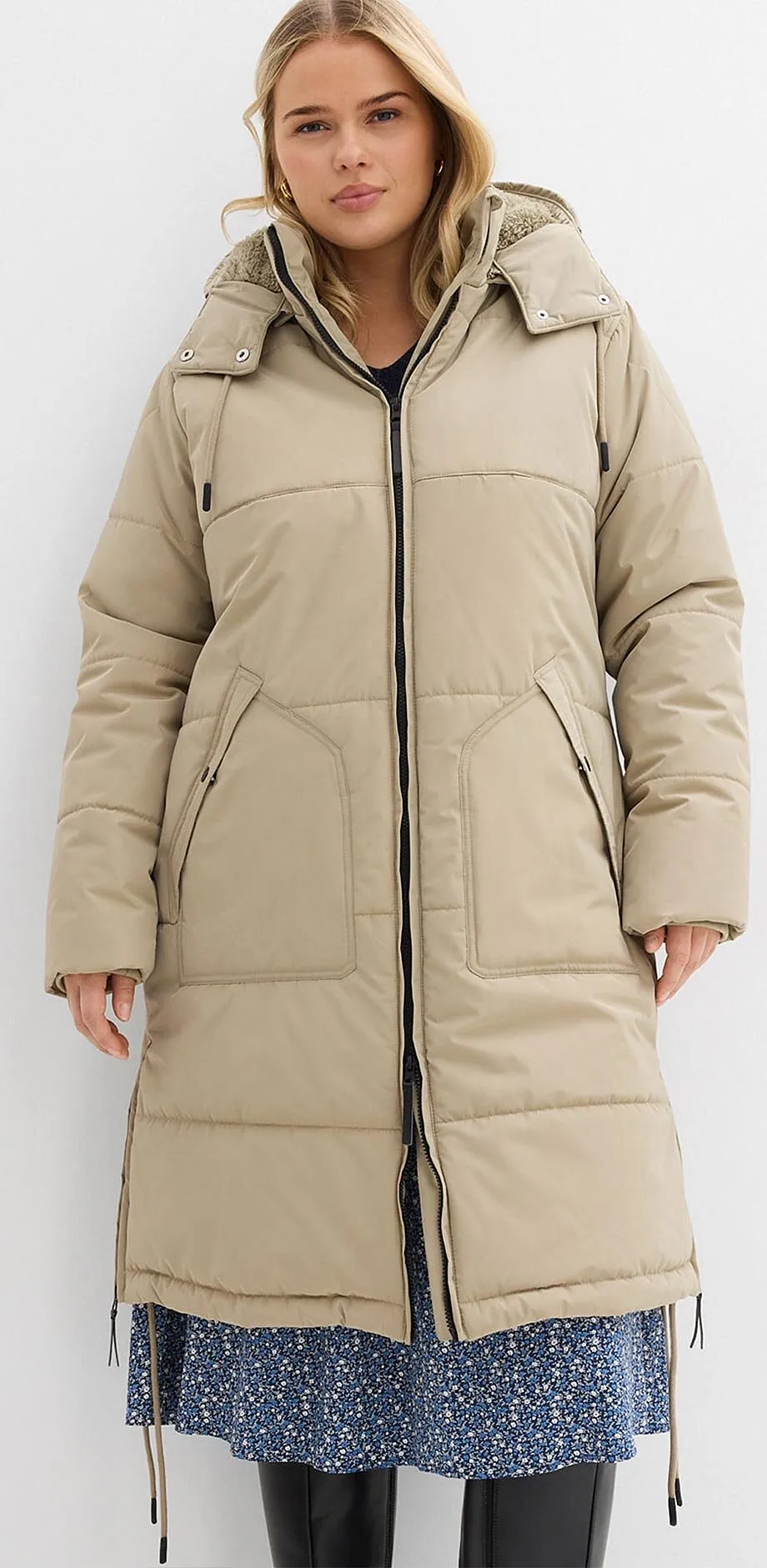 Manteau matelassé beige à capuche par dessus une robe bleue à fleurs.