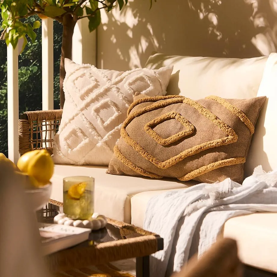 Salon de jardin ext&eacute;rieur cosy avec coussins de couleur claire et plaid douillet.