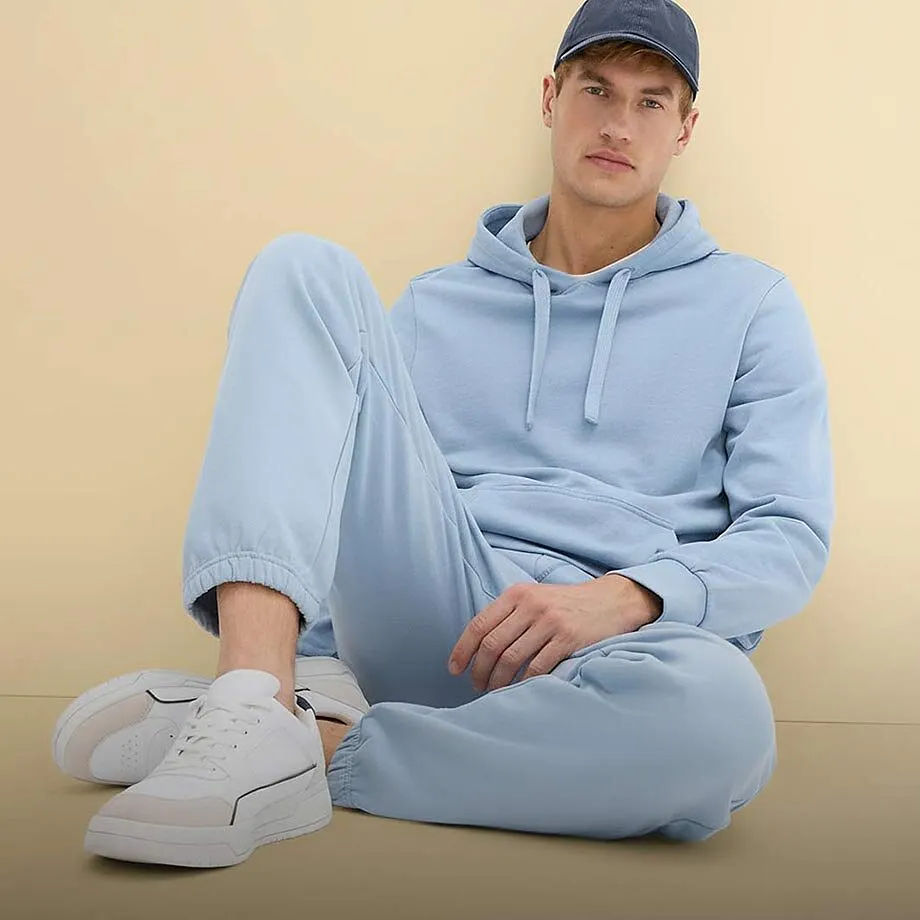 Sweat &agrave; capuche bleu clair et pantalon de jogging compl&eacute;t&eacute;s d'une paire de sneakers blanches et d'une casquette bleue.