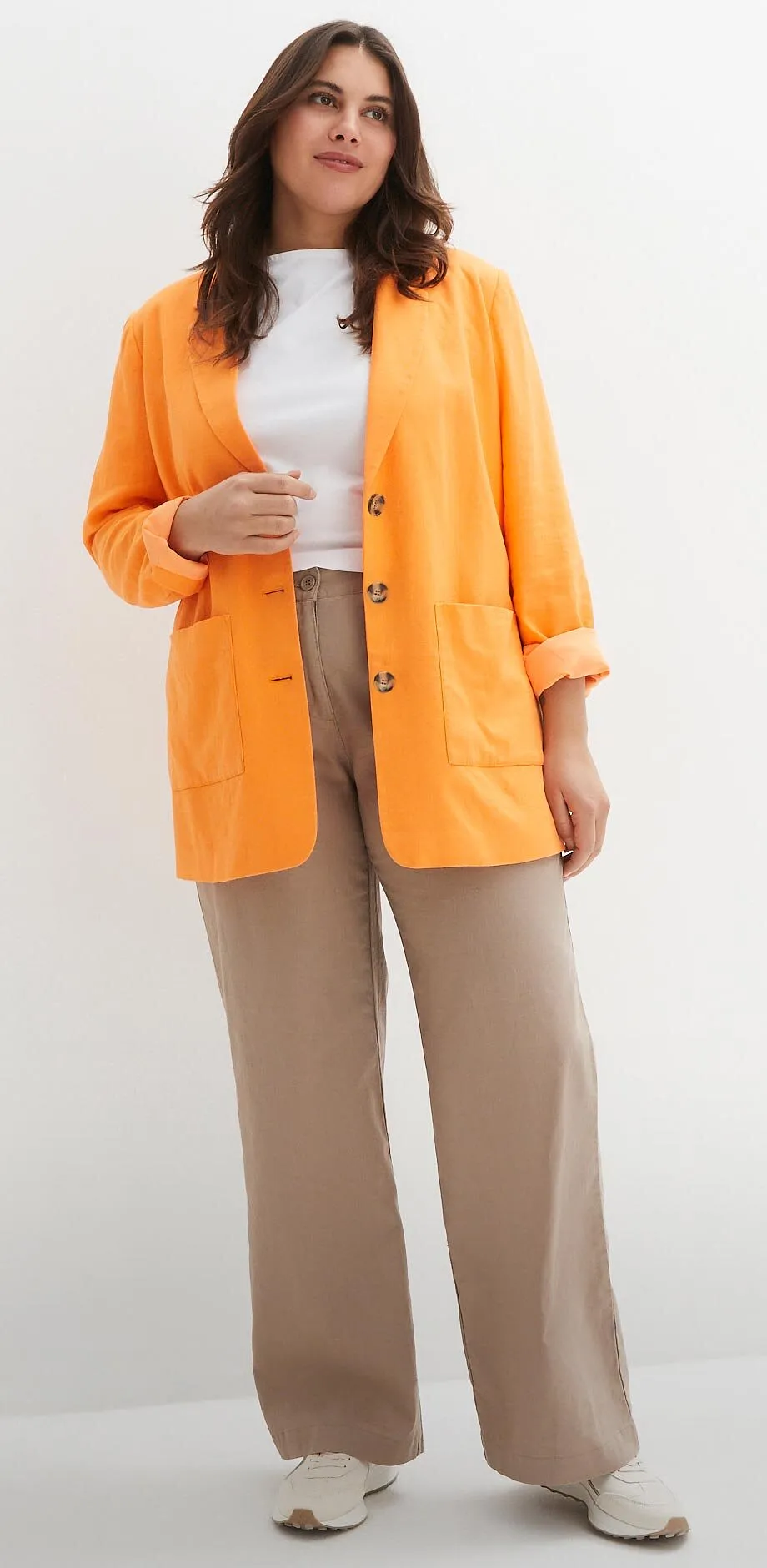 Cardigan orange sur un top blanc, pantalon beige et chaussures de couleur claire.