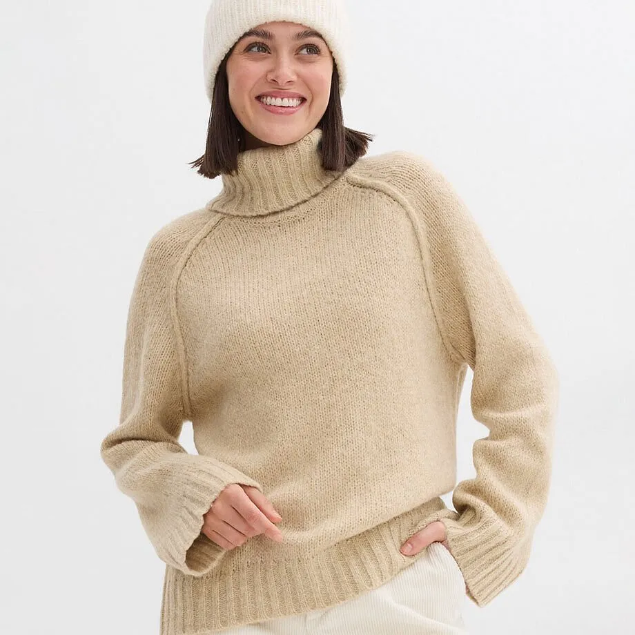 Pull douillet beige &agrave; col roul&eacute; avec bonnet blanc.
