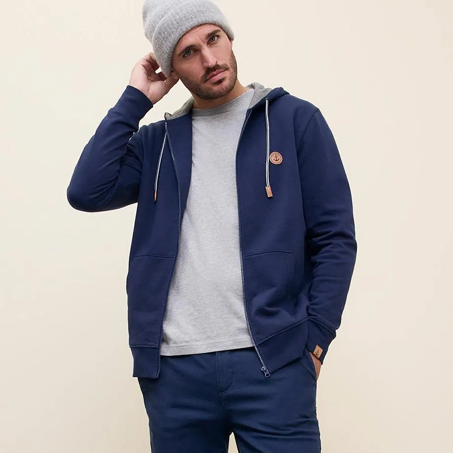 Look d&eacute;contract&eacute; avec gilet bleu &agrave; capuche, bonnet gris et pull clair.