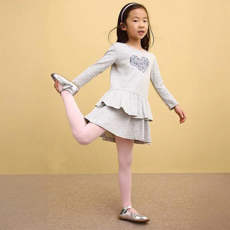 Une petite fille v&ecirc;tue d'une robe grise &agrave; volants et d'un collant rose.