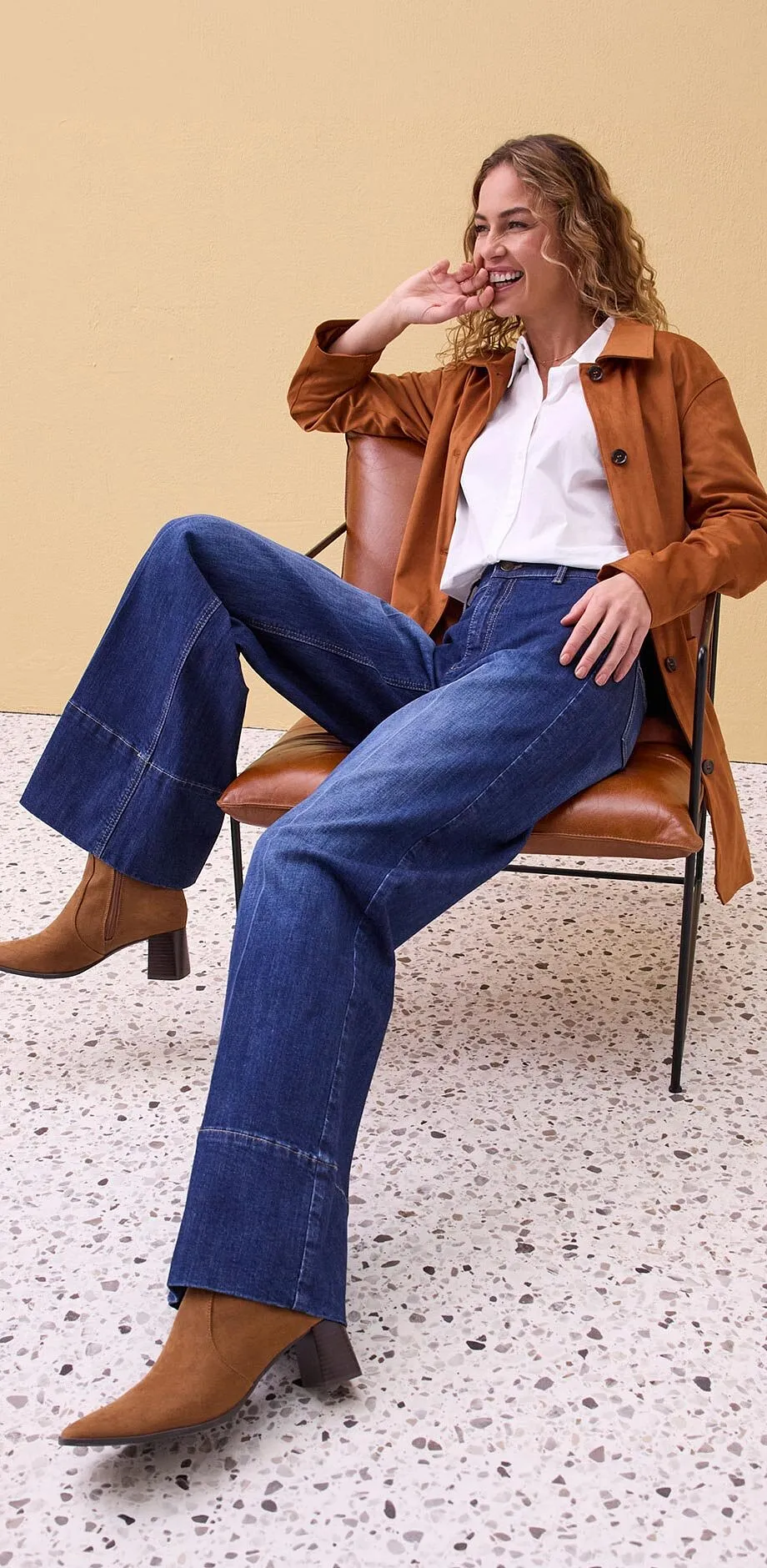 Veste enduite marron, chemisier blanc et jean de coupe large.